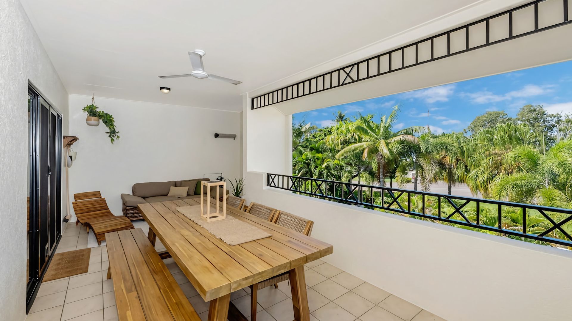A balcony with a wooden table and benches, a ceiling fan, and a view of a tropical landscape.