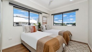 Un dormitorio con dos camas, un ventilador de techo y amplias ventanas con vistas a edificios.