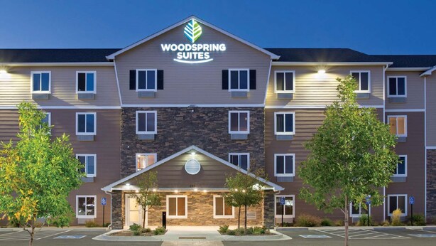 Un hotel de varios pisos con una entrada central, señalizada con un letrero que dice "Woodspring Suites".