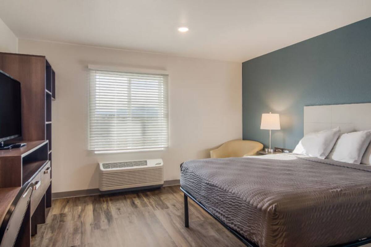 Ein Hotelzimmer mit Bett, Fernseher, Sessel und Fenster mit Jalousien.
