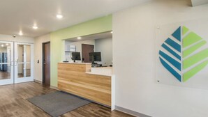 Un área de recepción con un mostrador de madera, alfombra gris y un logotipo montado en la pared.