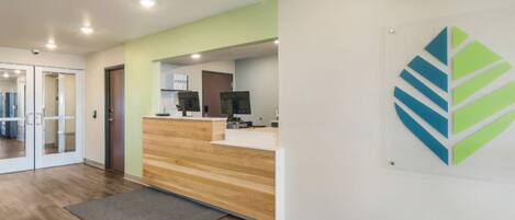 A reception area with a wooden reception desk, a grey carpet, and a wall-mounted logo.