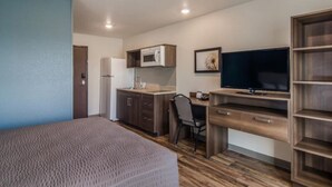 Habitación de hotel pequeña con cama, kitchenette, escritorio y televisor.