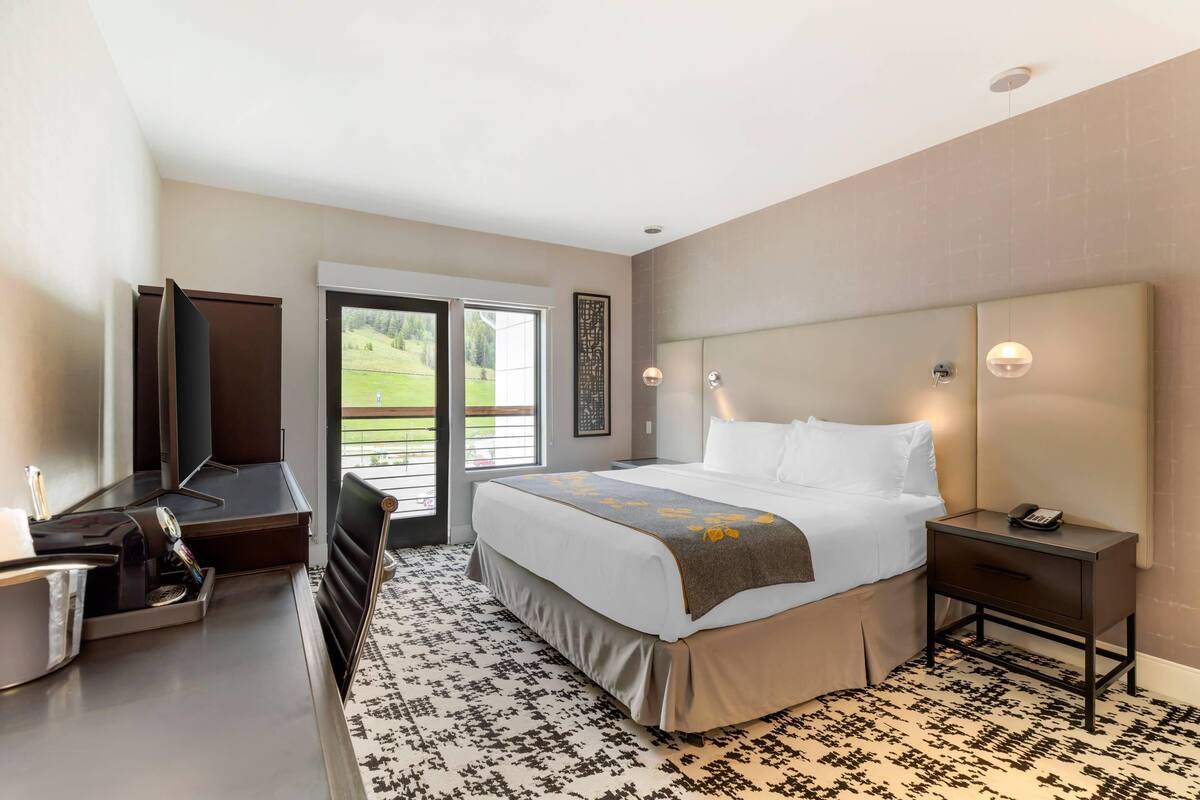 Een moderne hotelkamer met een groot bed, een bureau met een koffieapparaat, een televisie en uitzicht op een groen landschap.