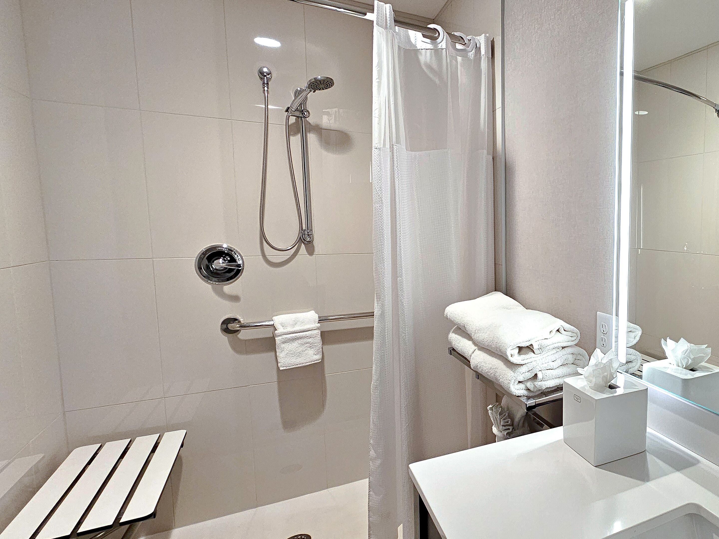 Un baño moderno con cabina de ducha de vidrio, un perchero y dispensador de papel higiénico.