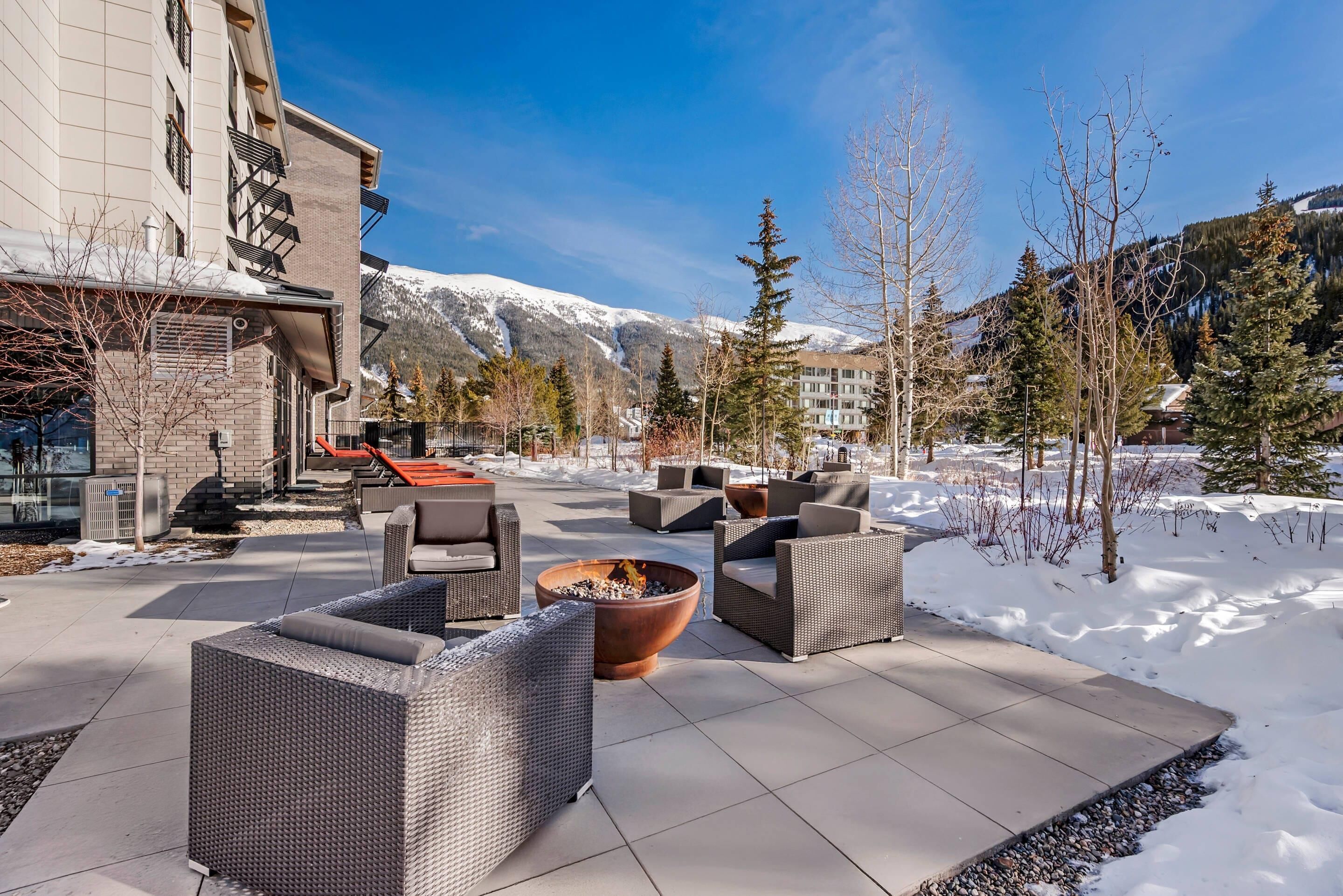 A patio area with outdoor furniture, a fire pit, and a view of snow-covered mountains.