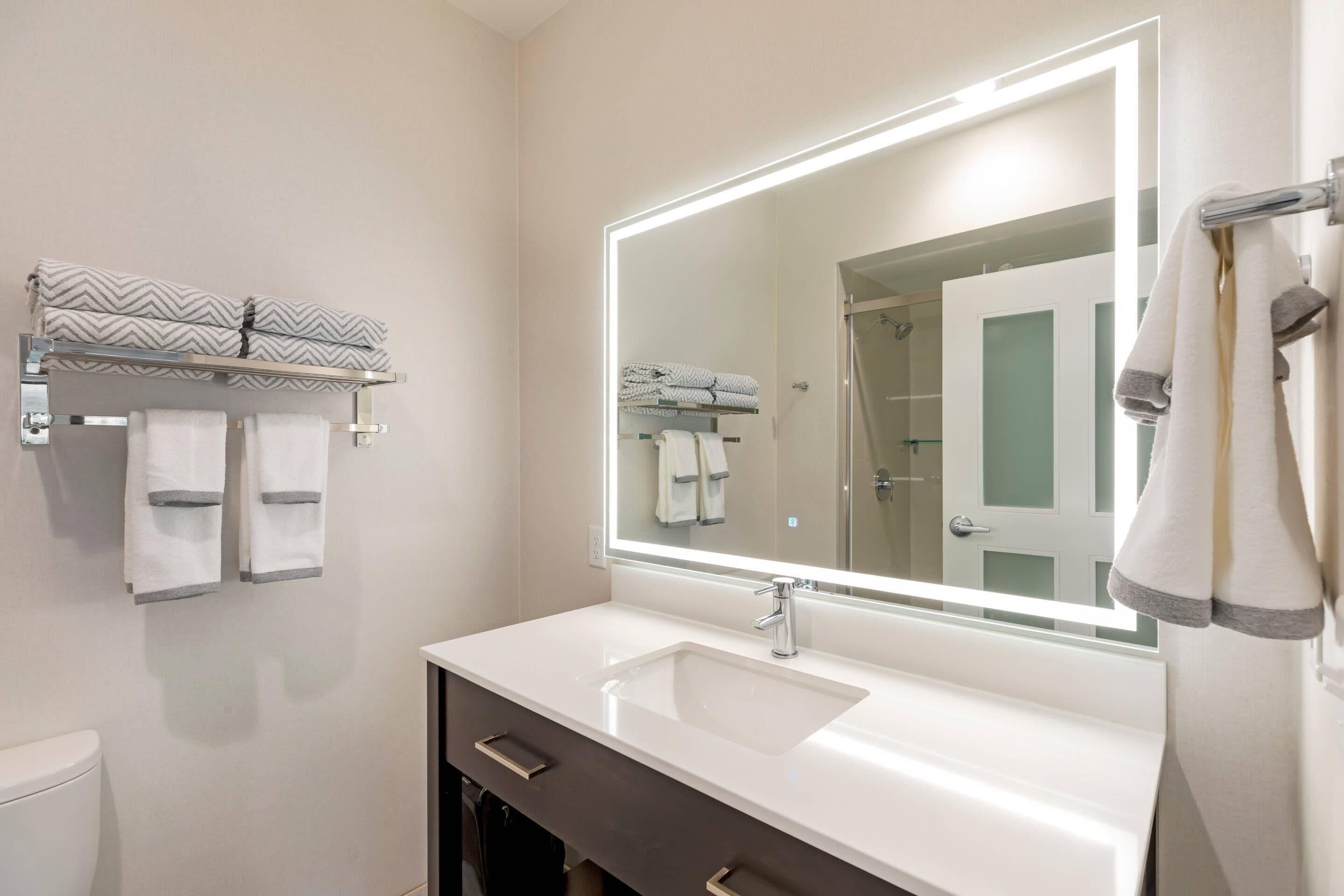 Une salle de bain avec un grand miroir, un lavabo blanc et un porte-serviettes.