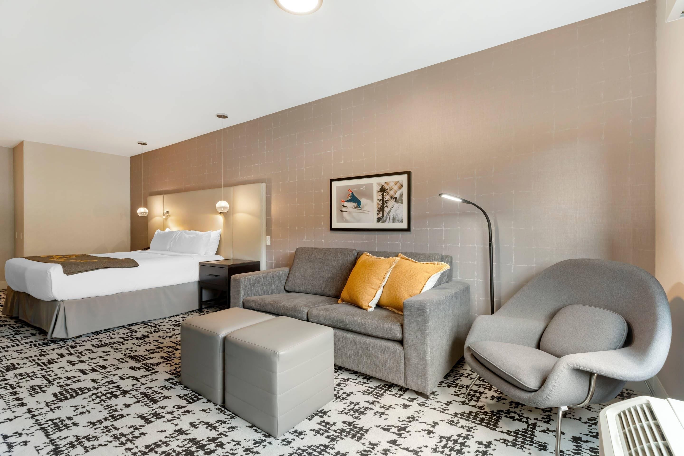 A hotel room with a bed, a sofa, a chair, a bedside table, and a wall-mounted picture.