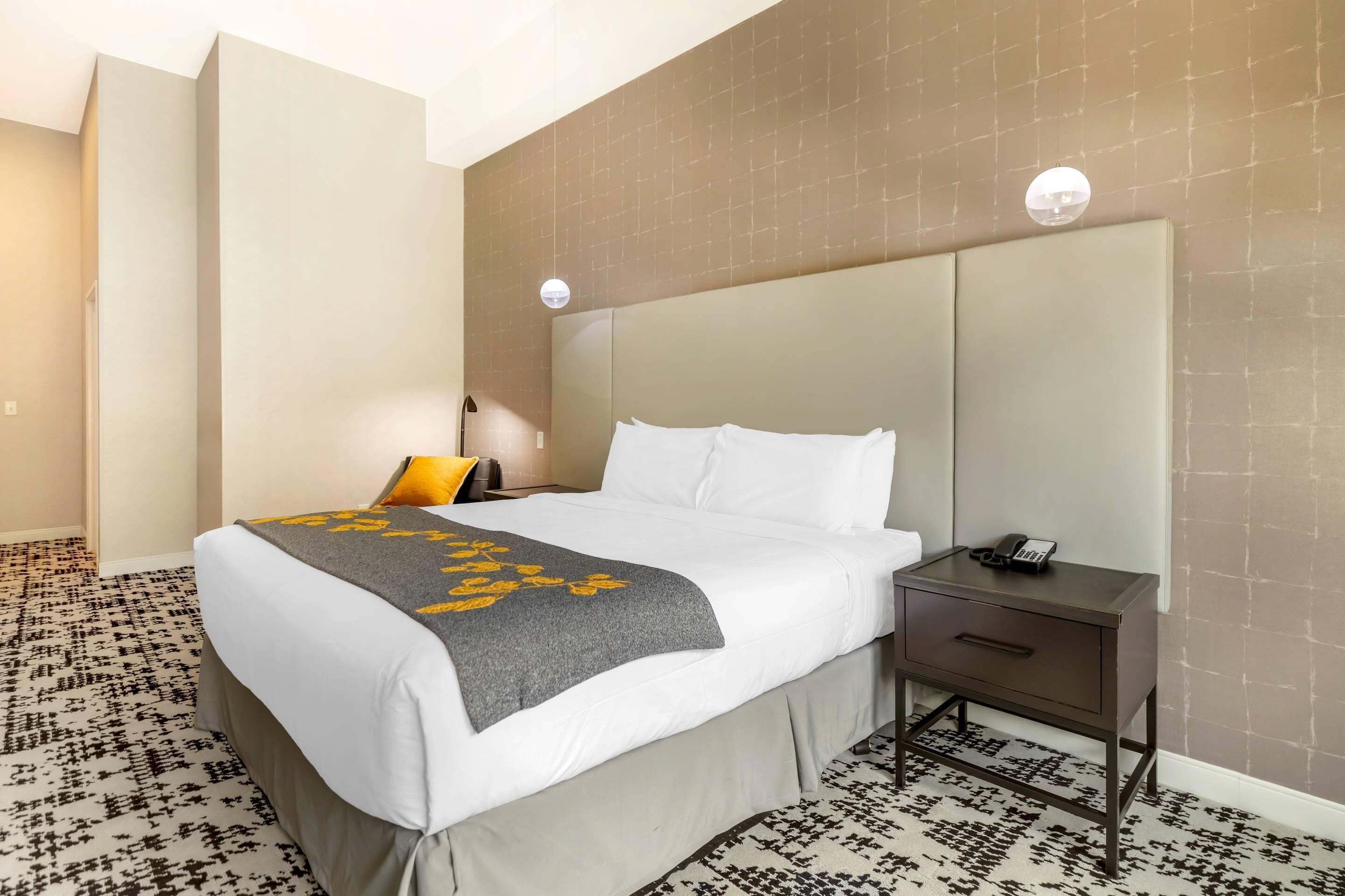A hotel room with a bed, bedside table, lamp, and patterned carpet.