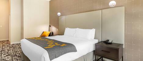 A hotel room with a bed, bedside table, lamp, and patterned carpet.