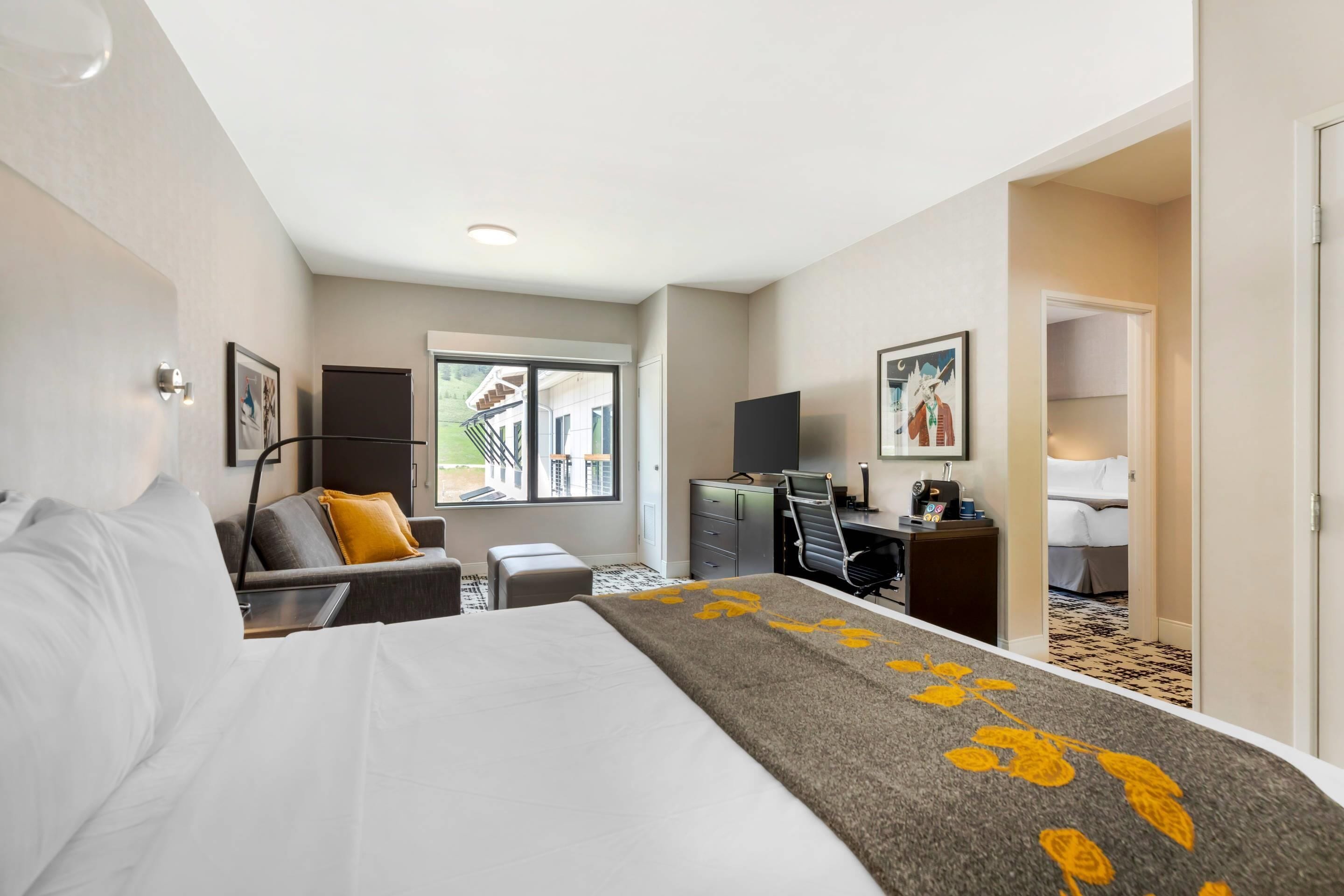 Habitación de hotel con cama, escritorio, sillón, televisión y ventana con vista a edificios.