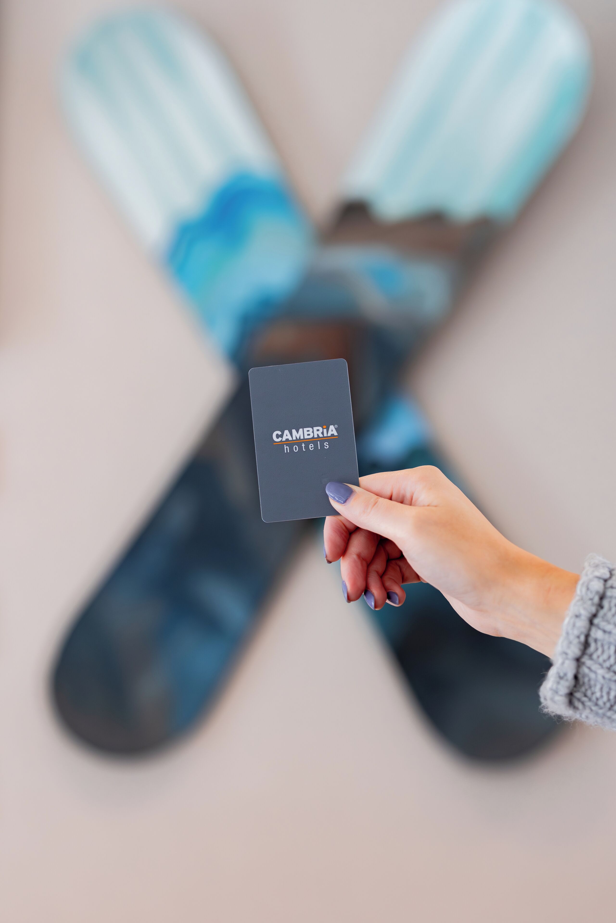En hand håller i ett kort med texten ”CAMBRIA hotels”, och i bakgrunden syns ett par skidor.