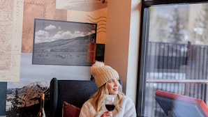Una persona sentada en una silla junto a una ventana, con una botella de vino, un mapa en la pared y una cesta de mimbre.