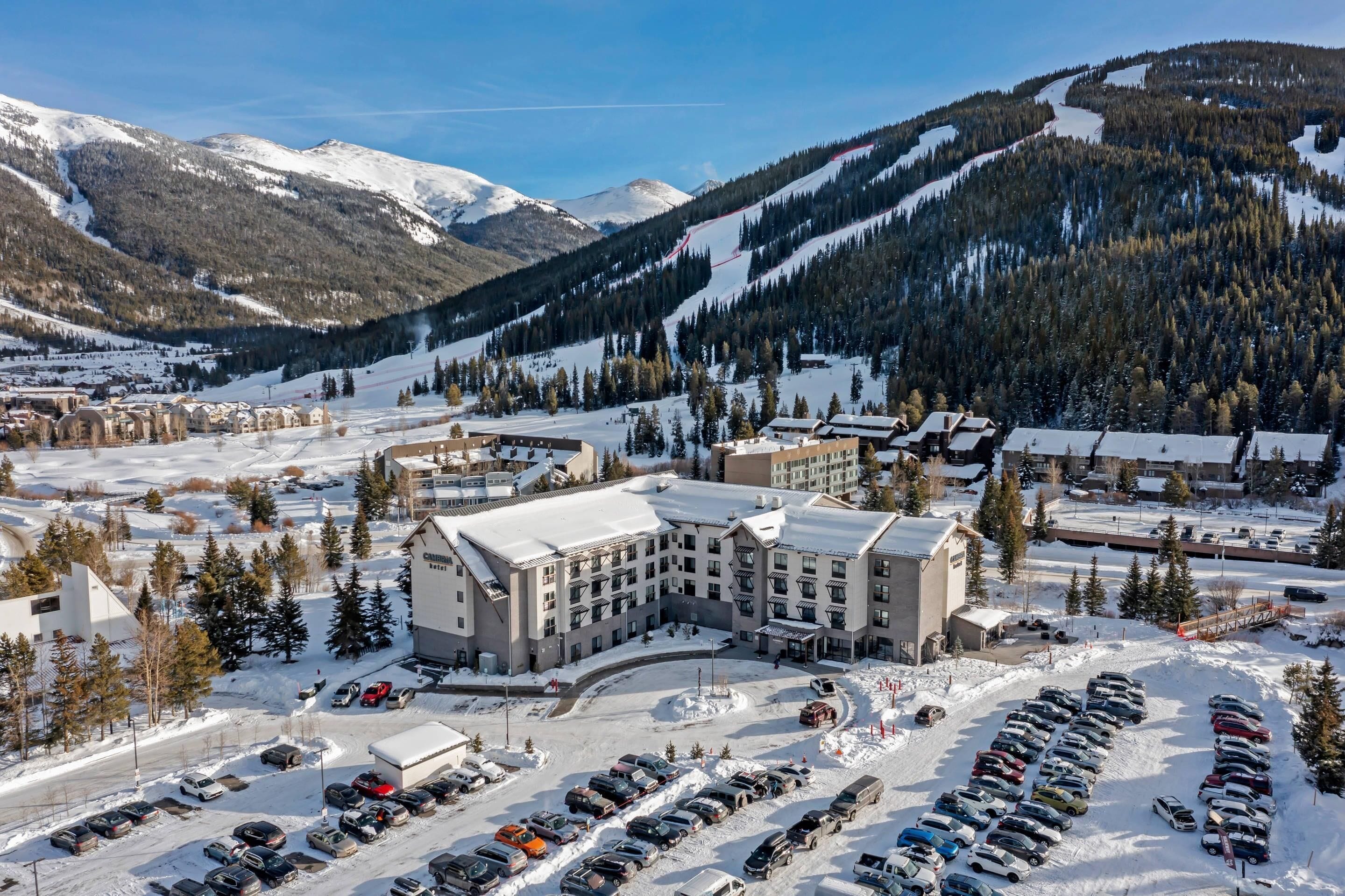 Un hotel con un patio central, rodeado de aparcamiento cubierto de nieve y un paisaje montañoso.