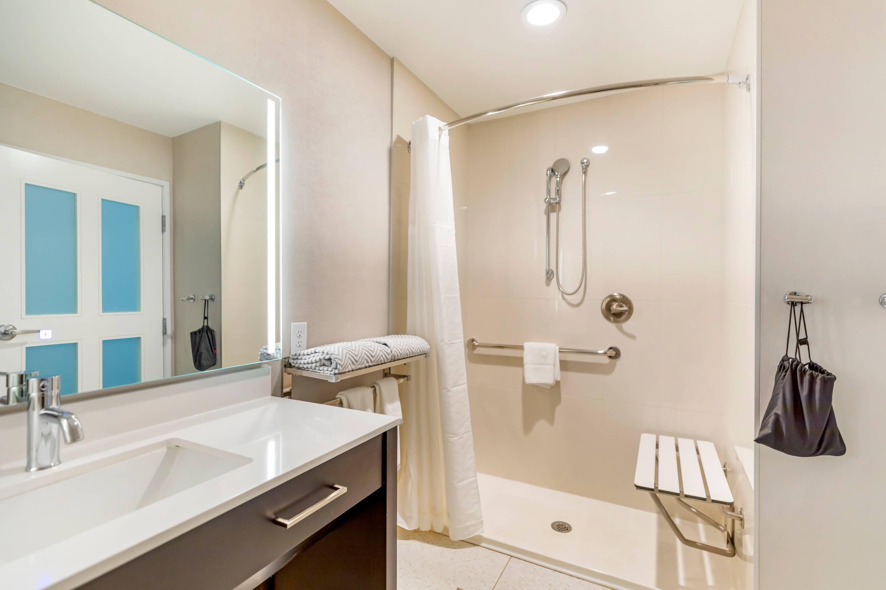 A bathroom with a white sink, a shower with a handheld showerhead, a towel rack, and a mirror.
