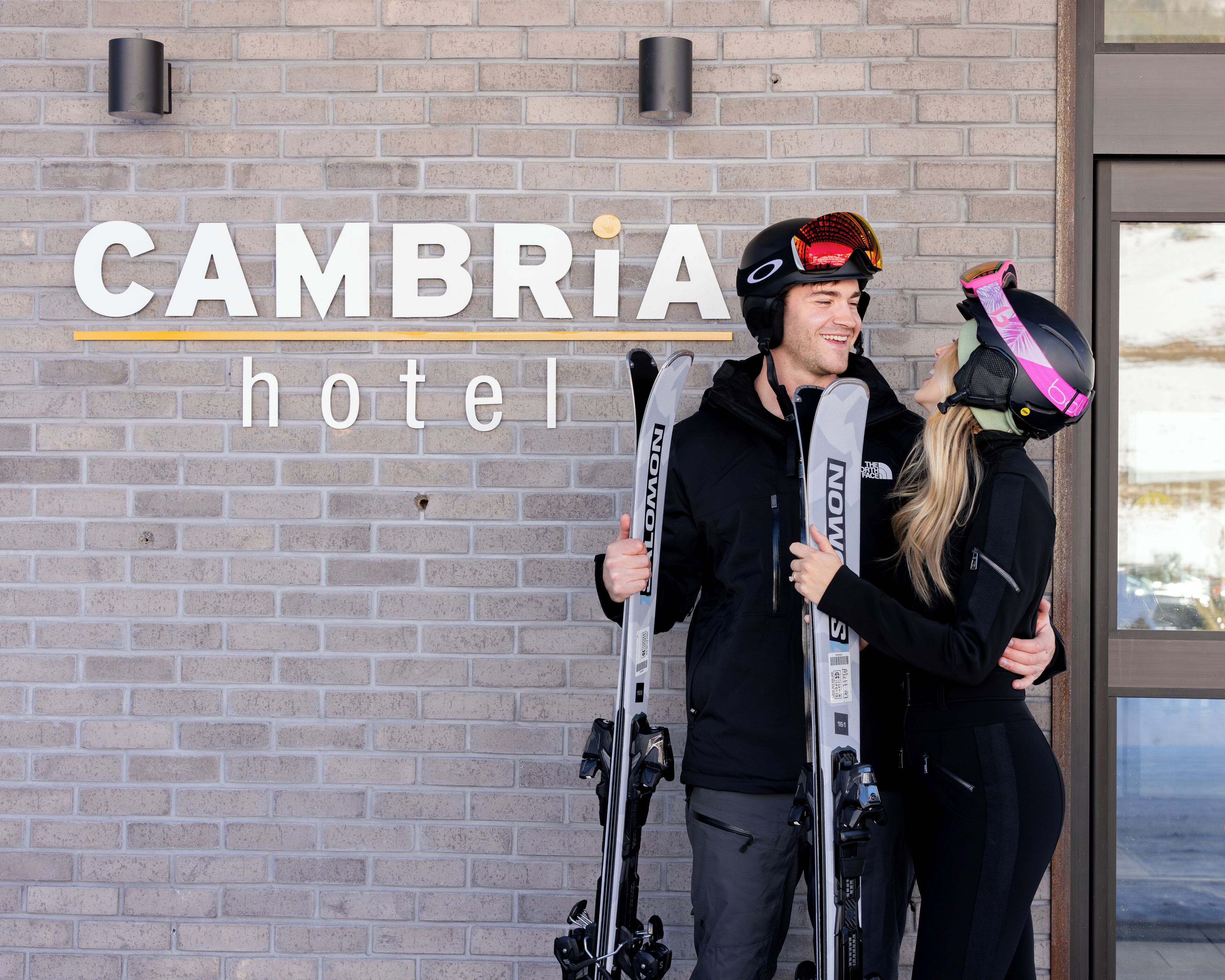 A brick wall with the text "CAMBRIA hotel" and two people holding skis.