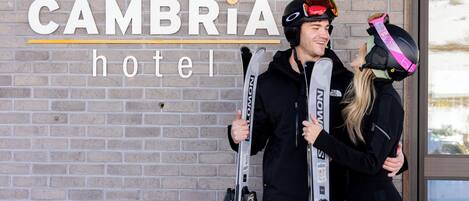 A brick wall with the text "CAMBRIA hotel" and two people holding skis.