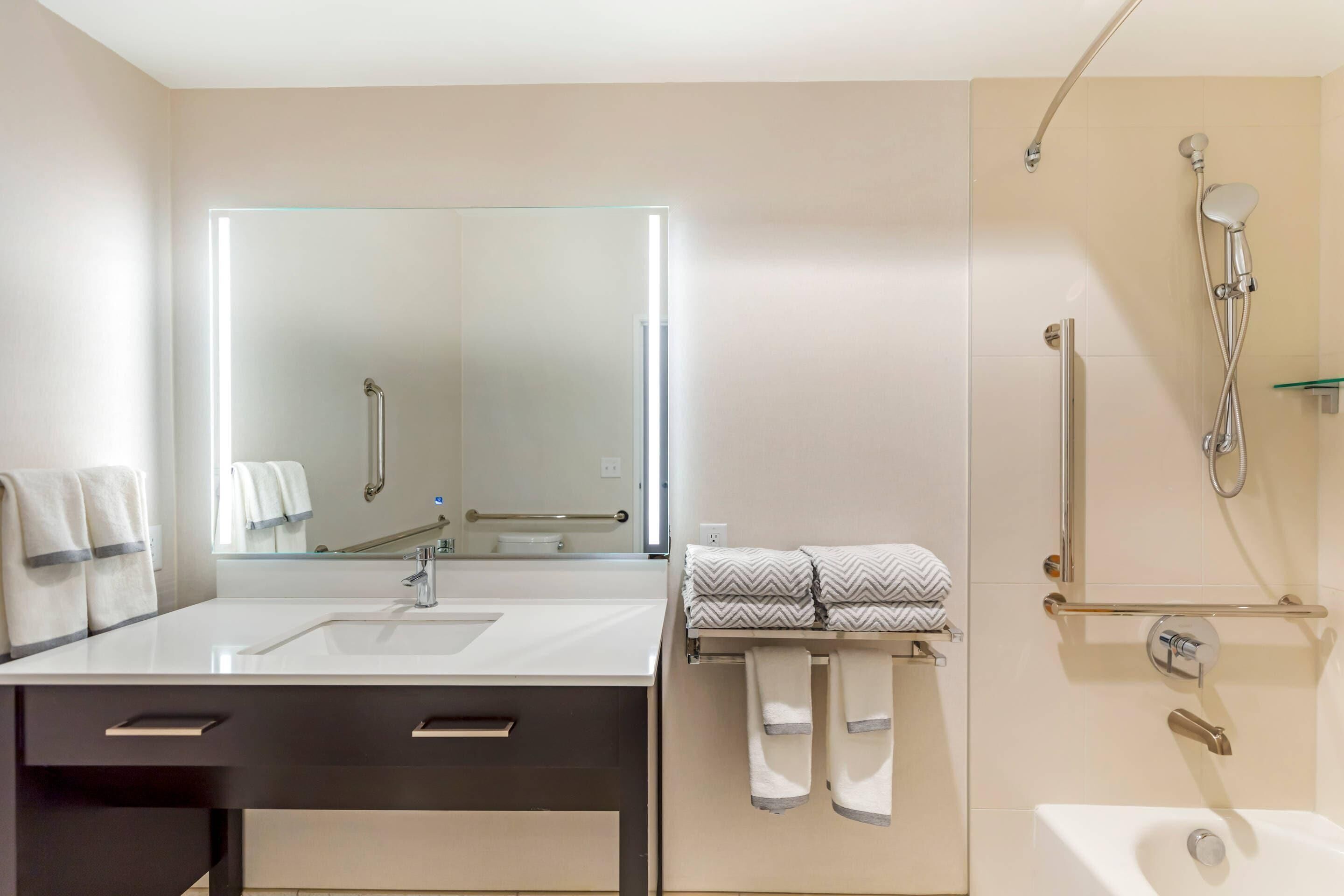 A modern bathroom with a large mirror, a sink, a bathtub, and a shower.