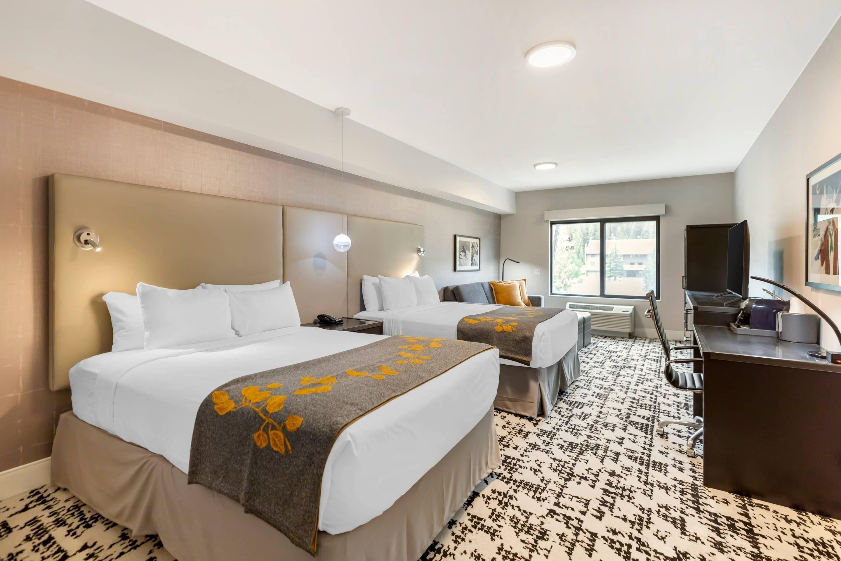 A hotel room with two beds, a desk, a chair, a TV, and a window.