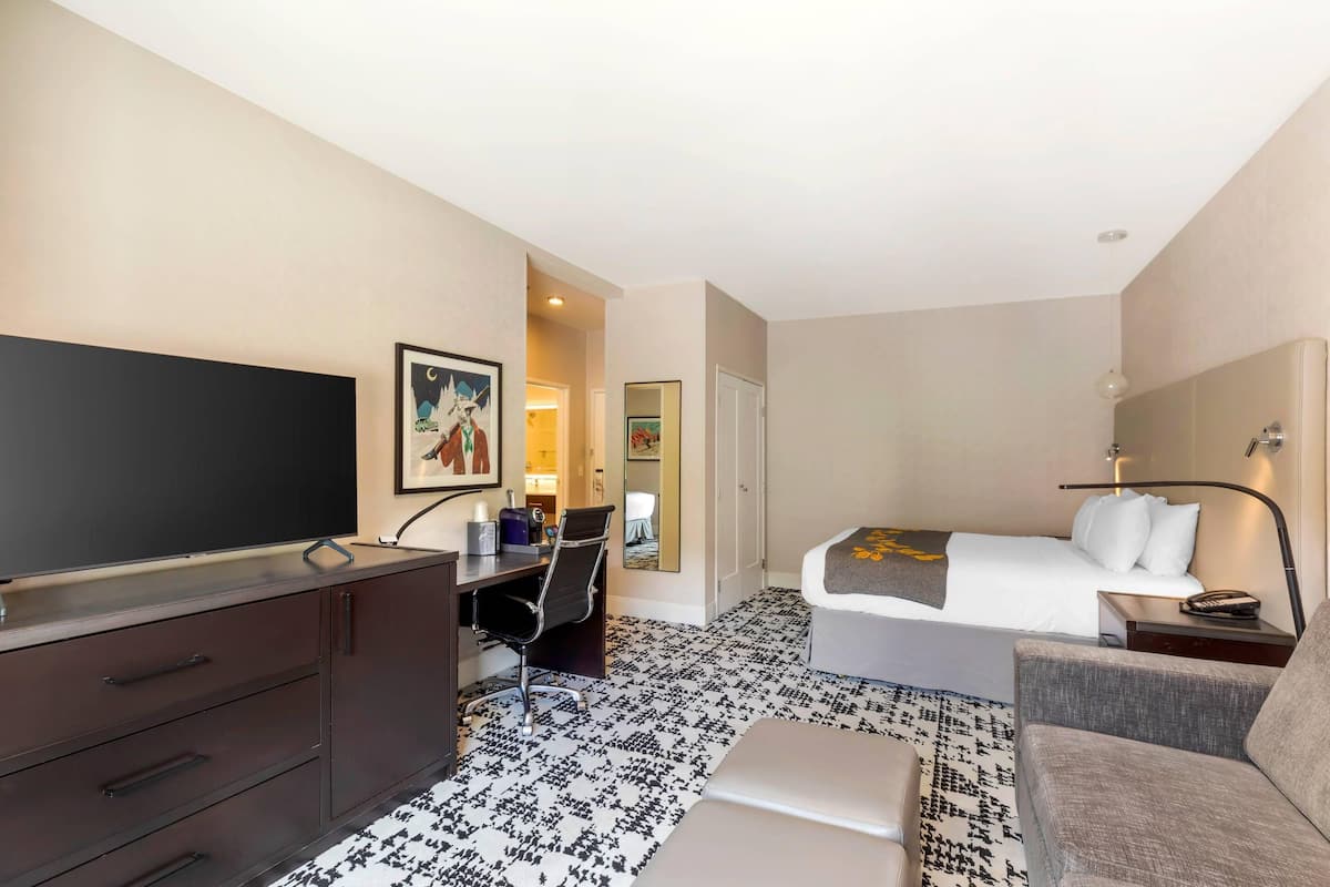 Een hotelkamer met een bed, een bureau met stoel, een televisie, een bank en een nachtkastje.