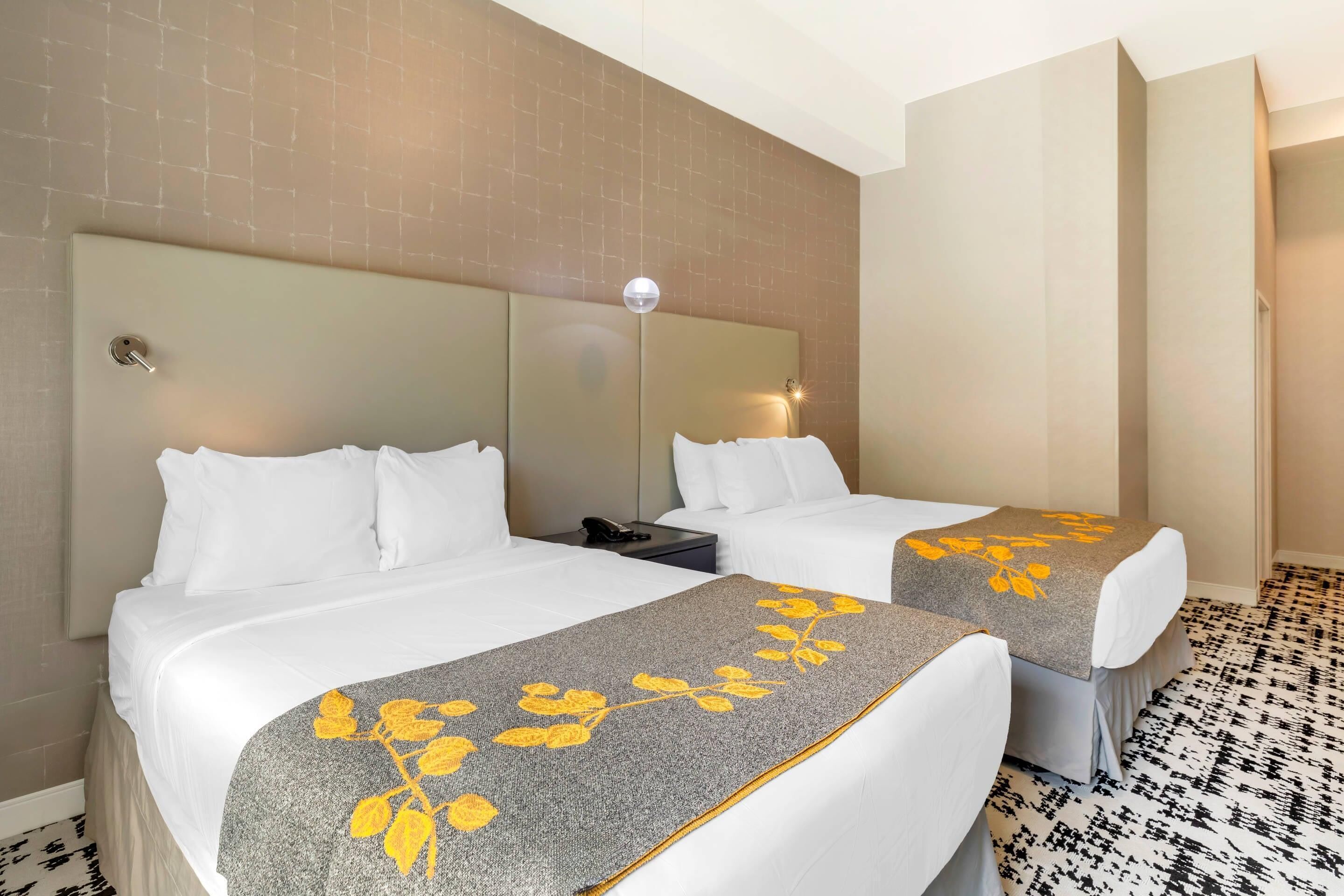 Ein Hotelzimmer mit zwei Betten, einem Nachttisch mit Lampe und einem gemusterten Boden.