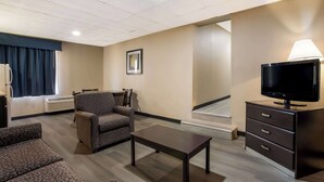 A hotel room with a sofa, armchair, TV, and a desk with drawers. - Suburban Studios Millville (Millville)
