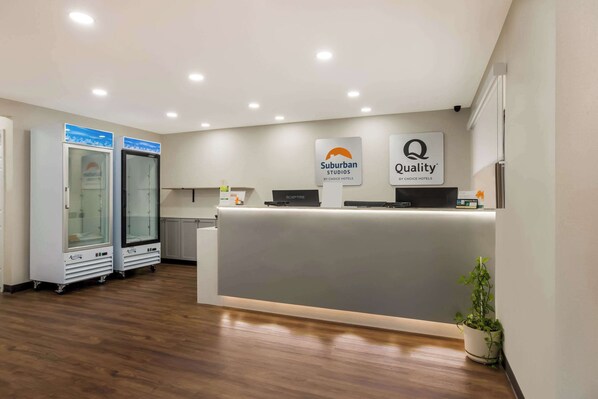 Zona de recepción de hotel con diseño moderno, que incluye un mostrador de recepción, dos vitrinas de vidrio y un letrero que indica 'Suburban Studios by Choice Hotels' y 'Quality'.