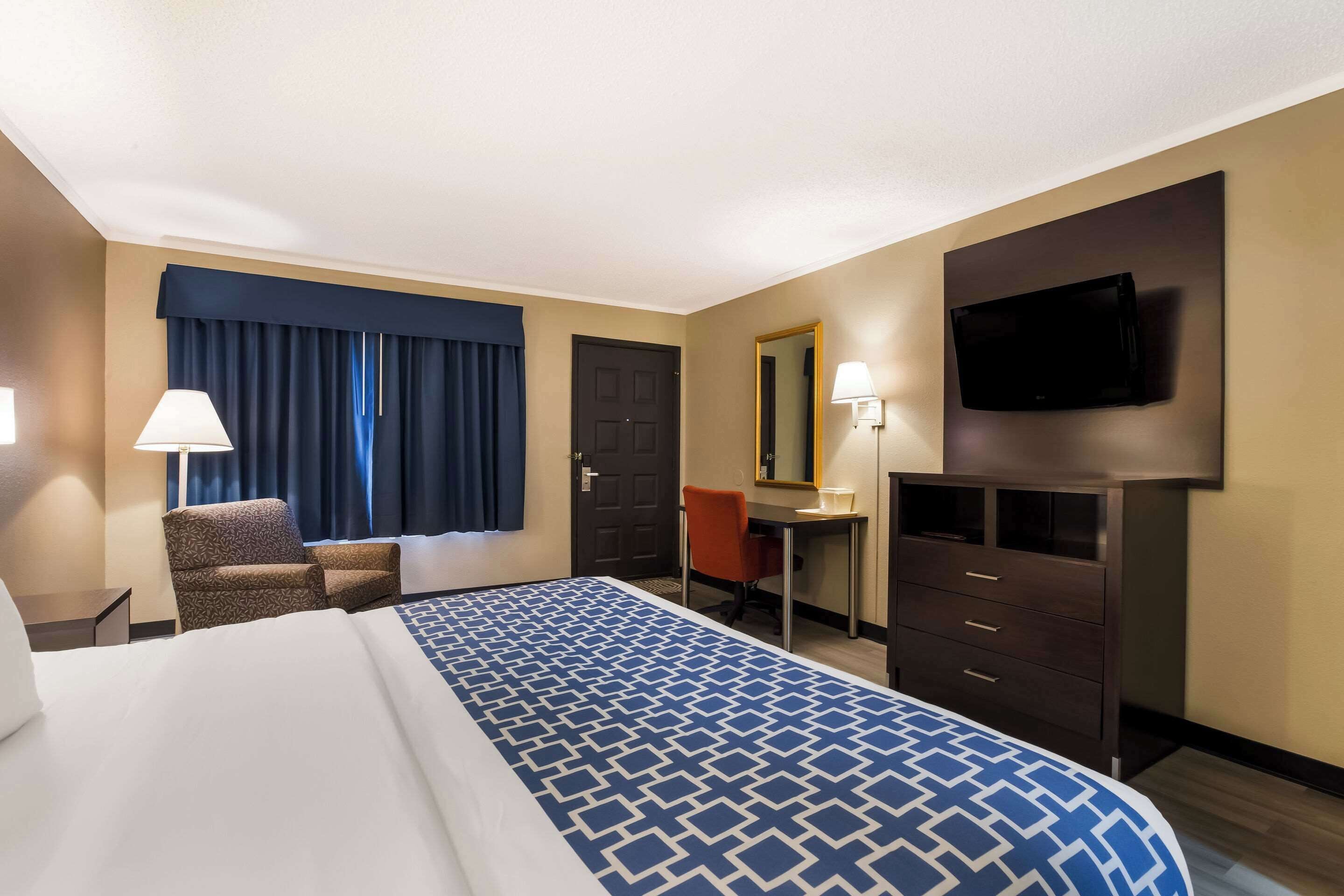Una habitación de hotel con una cama grande, un escritorio, una silla, un televisor y un aparador.