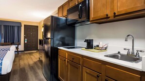 A compact kitchen with wooden cabinets, a black refrigerator, a microwave, and a sink. - Suburban Studios Millville (Millville)