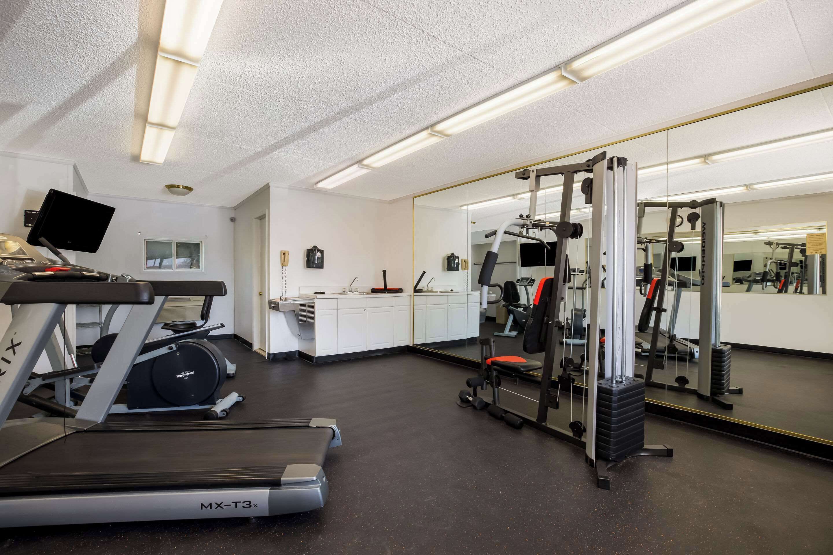 Ein Fitnessstudio mit Cardiogeräten, Krafttrainingsgeräten und einer Spiegelwand.