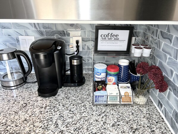 A kitchen counter with a coffee maker, a kettle, and a coffee station with various coffee products and a framed coffee definition sign. - Luxury-Lucky Fortuna Suite (Elk Grove)