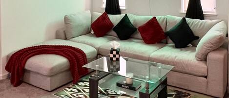 Una sala de estar con un sofá color beige, cojines rojos y negros, una mesa de centro de vidrio y un letrero de neón que dice "Future Suite".