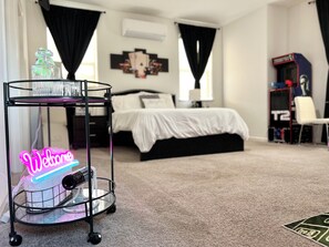 A bedroom with a bed, a neon 'Welcome' sign, a small table with a water bottle, and a T2 gaming console. - Luxury-Lucky Fortuna Suite (Elk Grove)