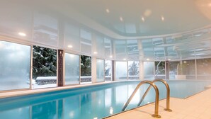 An indoor swimming pool with clear glass walls, a tiled floor, and metal handrails.