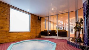 A spa room with a hot tub, wooden walls, large windows, and a tiled floor.