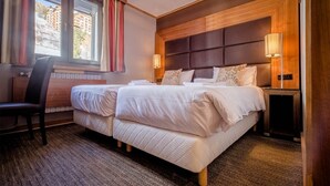 A double bed with a wooden headboard, two bedside lamps, a chair, and a view of a building outside.