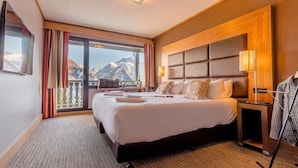 A hotel room with a large bed, a nightstand, a lamp, and a view of mountains.