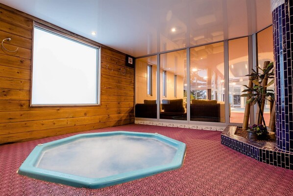 A spa room with a hot tub, wooden walls, large windows, and a tiled floor.
