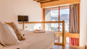 Un dormitorio con una cama litera de madera, un televisor montado en la pared y una ventana con vistas a un paisaje montañoso nevado.