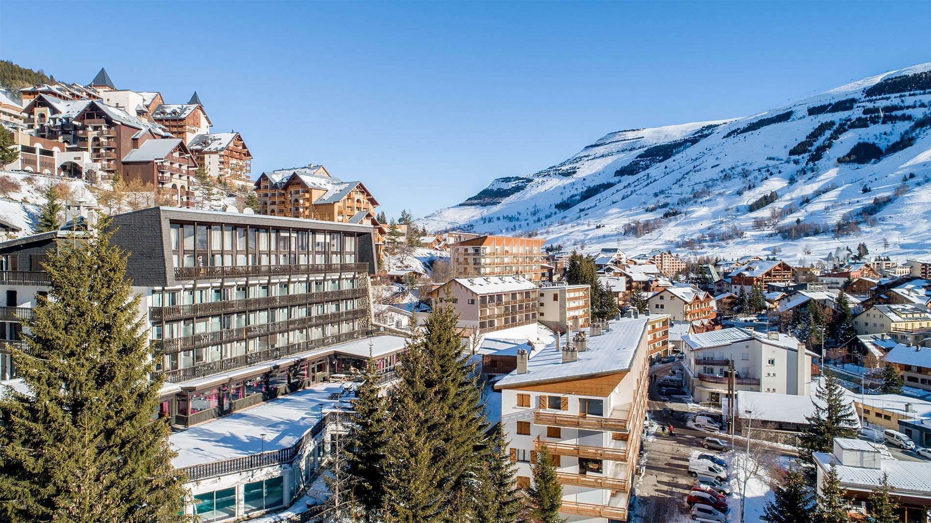 Un pueblo nevado en la montaña con edificios de madera tradicionales y construcciones modernas, con una combinación de balcones y grandes ventanales.