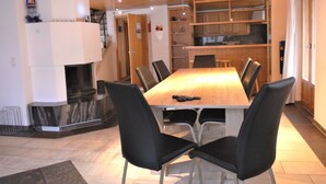 Un espace de salle à manger moderne avec une table en bois et des chaises noires, une cheminée et une cuisine en arrière-plan.