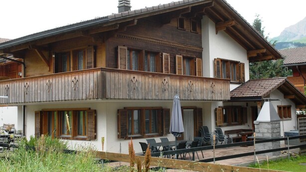 Un chalet à deux étages doté d’un balcon, d’un espace extérieur aménagé et d’une cheminée en pierre.