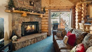 Interior d'una cabana de fusta amb una llar de pedra, un sofà amb coixins estampats i un sostre de fusta.