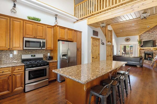 A spacious kitchen with granite countertops, wooden cabinets, stainless steel appliances, and a large island with bar stools.
