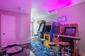 Um quarto com jogos de fliperama, um letreiro neon e um chão com padrão de estrelas.