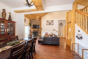 A wooden interior with a dining area, a fireplace, a sofa, and a staircase.