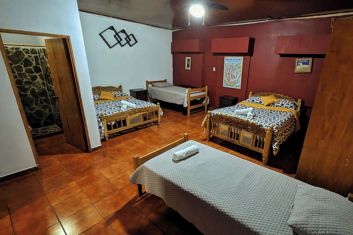 Une pièce avec deux lits en bois, une petite table et une chaise. Il y a une affiche accrochée au mur et une porte qui donne sur une autre pièce.