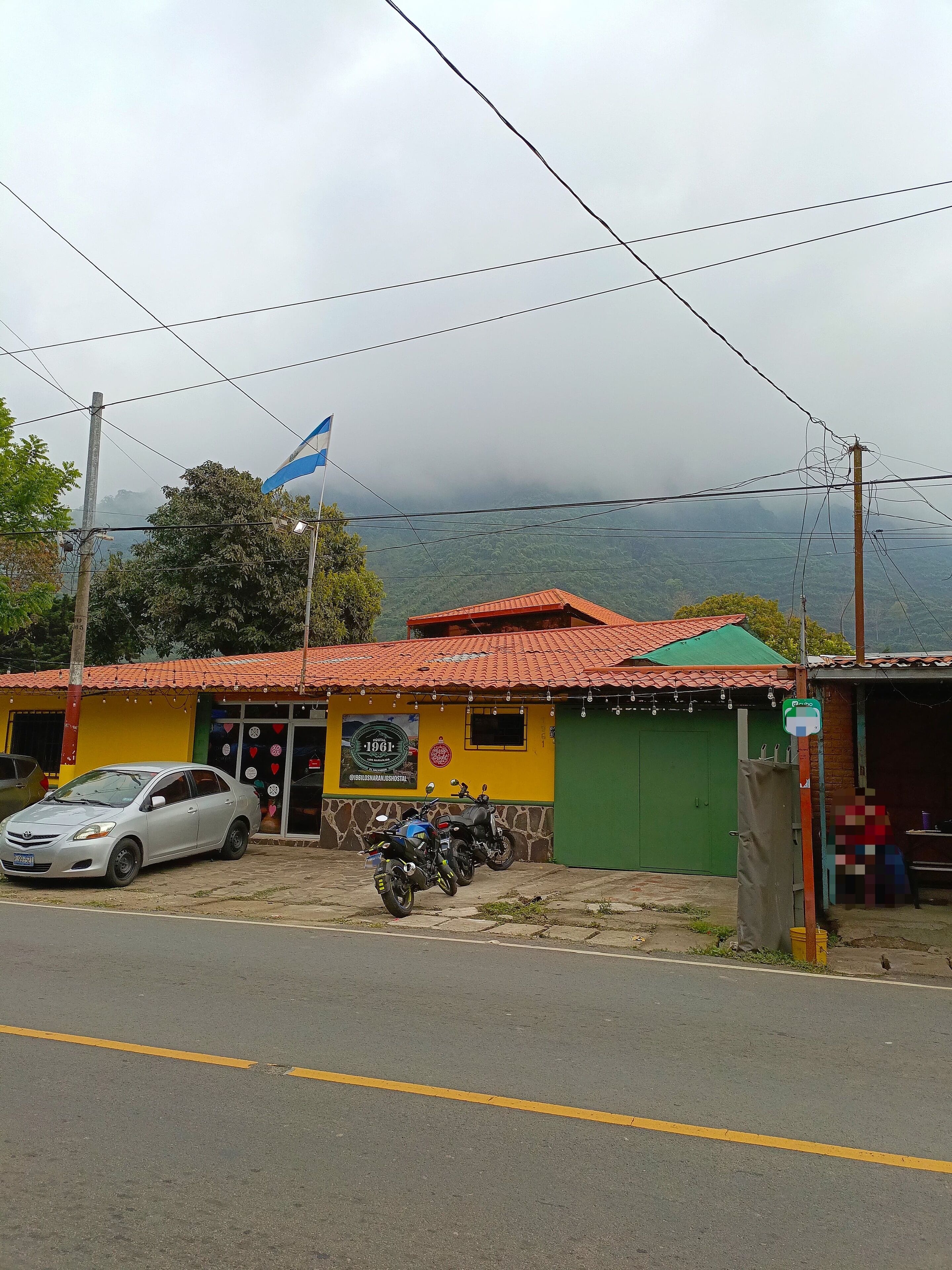 A building with a red-tiled roof, a parked car, and two motorcycles in front.