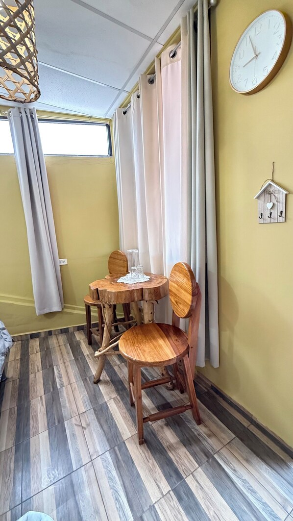 A room with a wooden dining table and chairs, a wall clock, and a window with curtains. - 1961 Los Naranjos Hostal (Juayua)