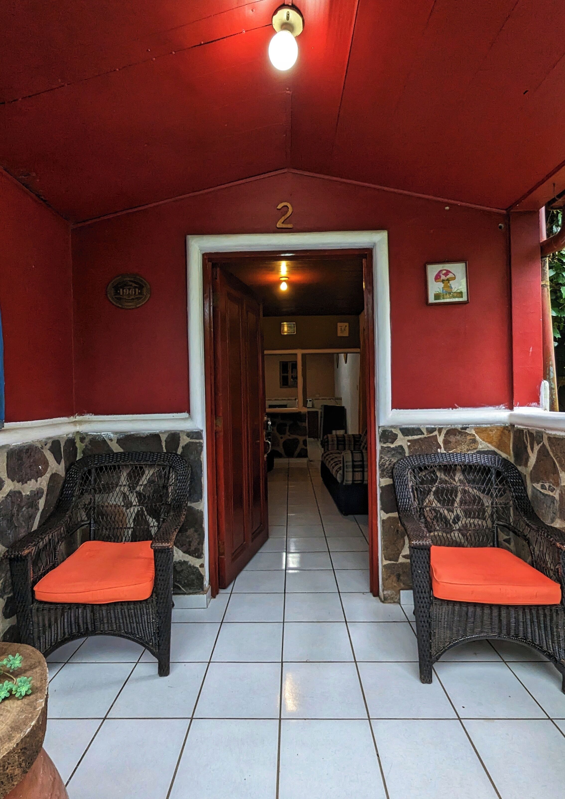A covered outdoor seating area with wicker chairs and stone walls, leading to a doorway marked with the number 2.